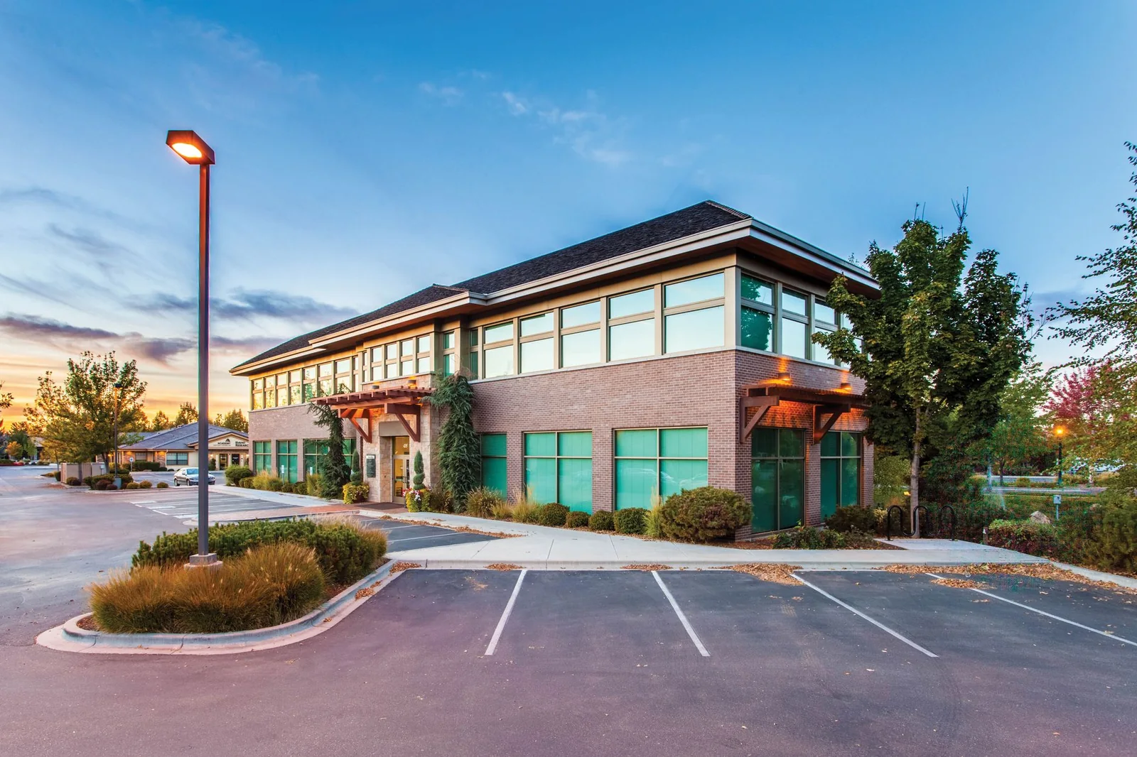 Immeuble de bureaux de deux étages en brique avec stationnement, au crépuscule.