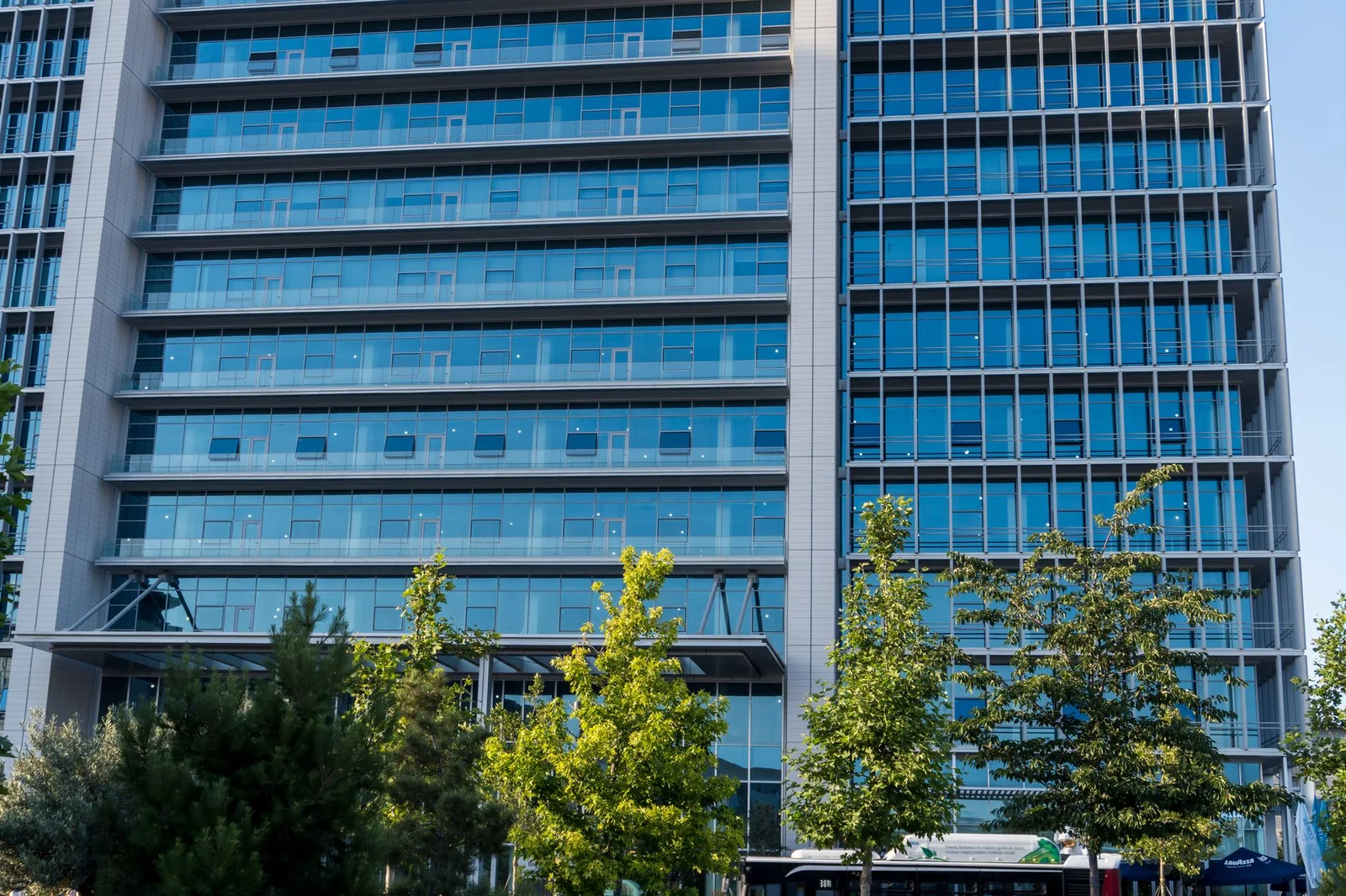Façade vitrée d'un immeuble de bureaux moderne, bordée d'arbres.